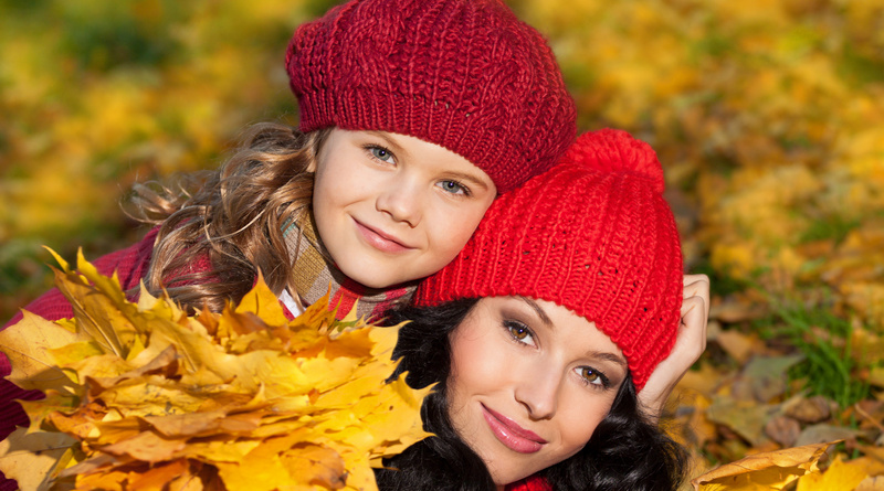 attractive young caucasian woman and girl in warm colorful clothing  lying on yellow leaves outdoors smiling