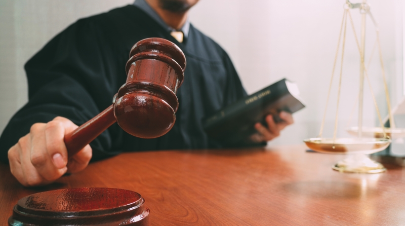 justice and law concept.Male judge in a courtroom with the gavel and working with smart phone and brass scale on wood table