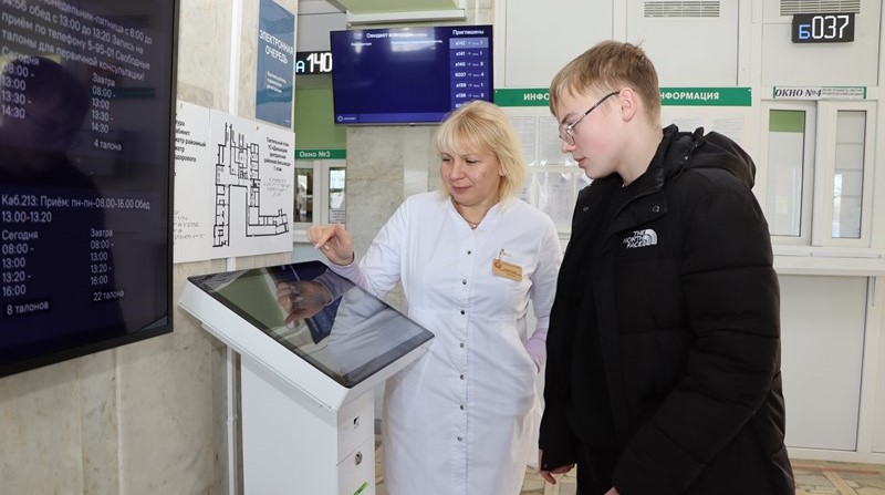 Вольга Камінская кансультуе пацыента ля тэрмінала электроннай чаргі.